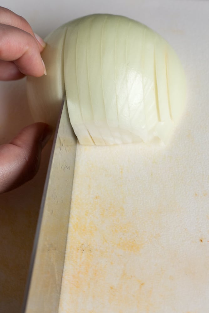 A hand chopping an onion on a white cutting board with a large sharp knife.