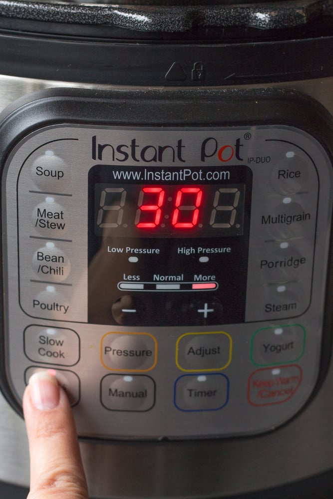 A finger pressing the saute button on an Instant Pot to turn it on.