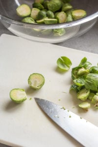 cutting brussels sprouts on a cutting board with a knife