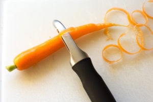 peel carrots with peeler on cutting board