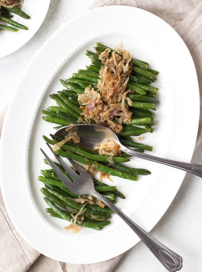 green beans on a white platter with serving utensils
