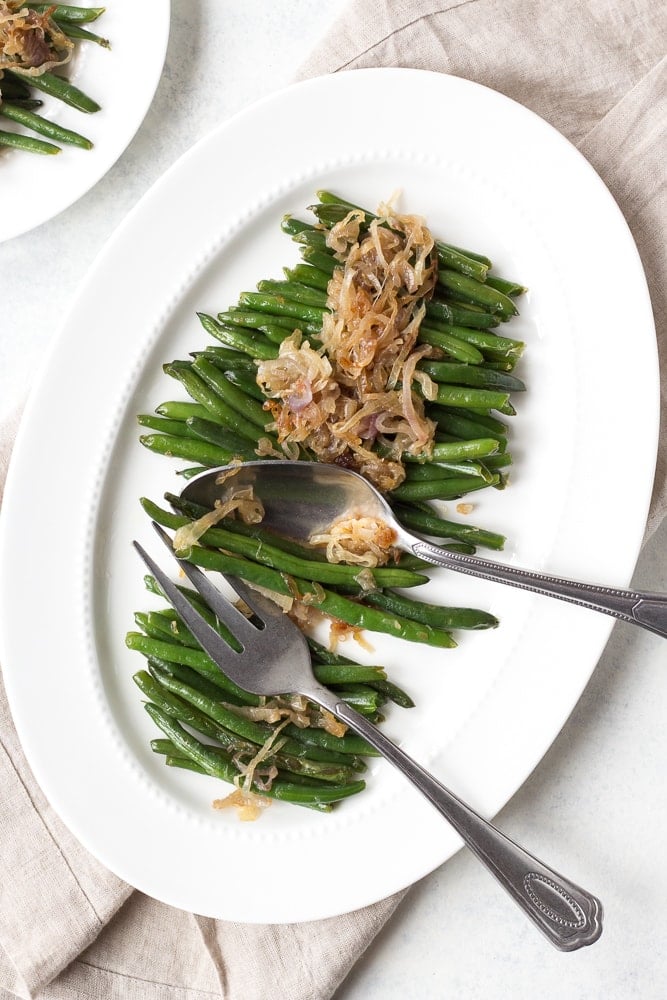 green beans on a white platter with serving utensils