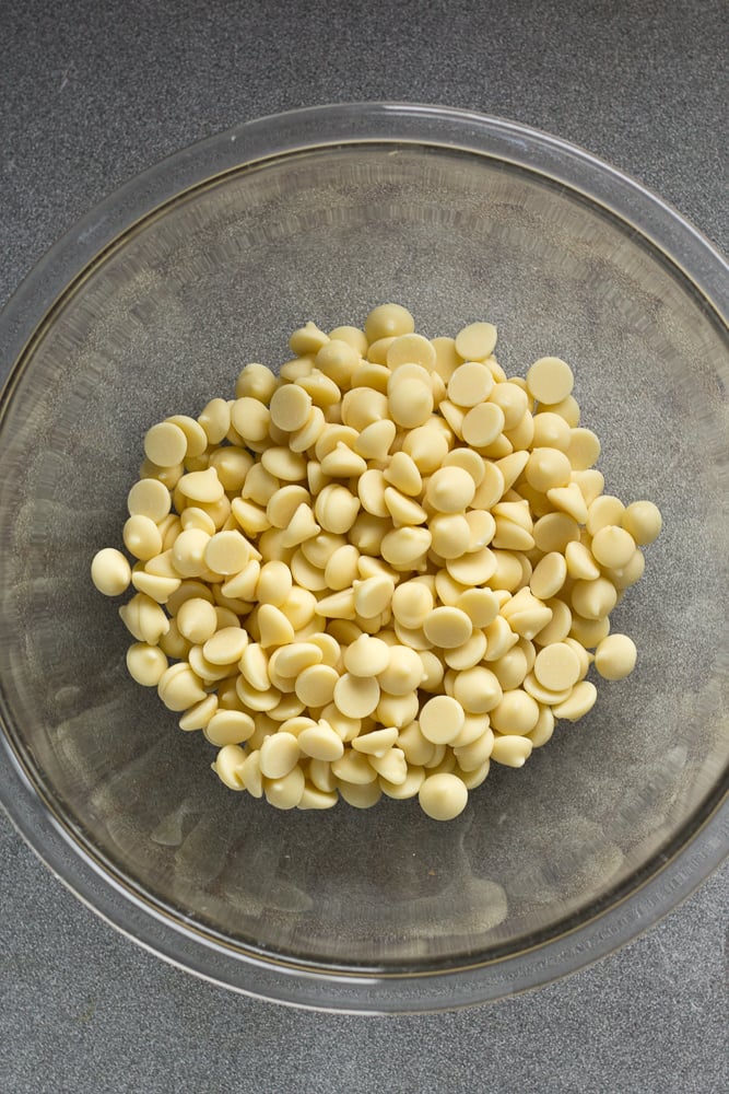 A clear bowl with white chocolate chips in it on a gray background.