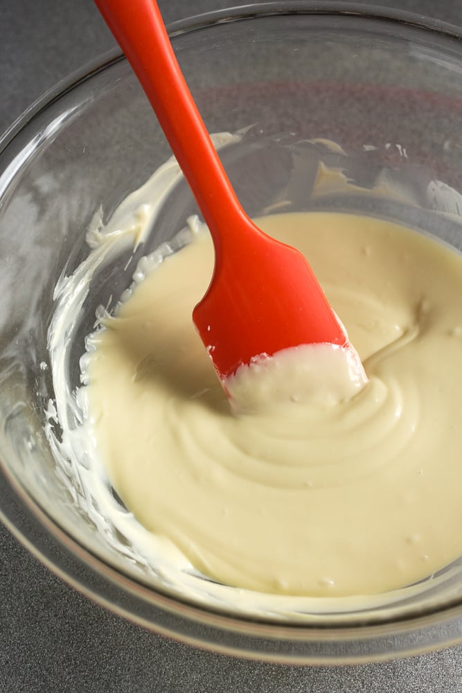 Melted white chocolate in a bowl with a red spatula.