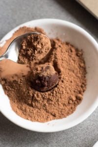 spooning cacao powder over a chocolate truffle