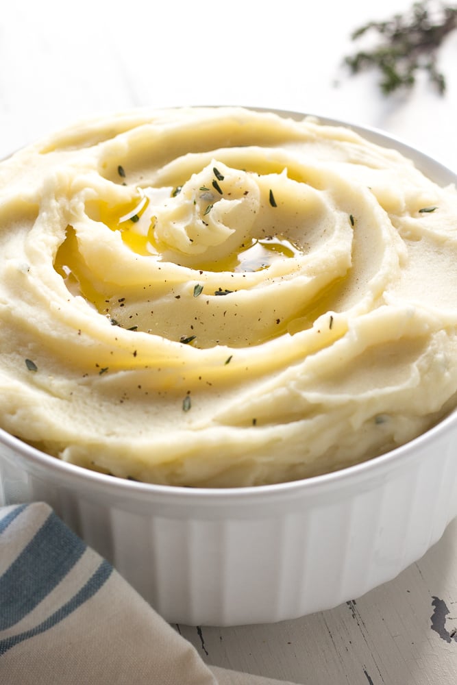 a bowl of whole30 mashed potatoes with thyme sprigs and a towel nearby