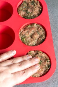 pressing paleo meatloaf muffins into red silicone muffin tin