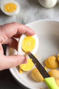 wedging an egg yolk out of a hard boiled egg with a knife