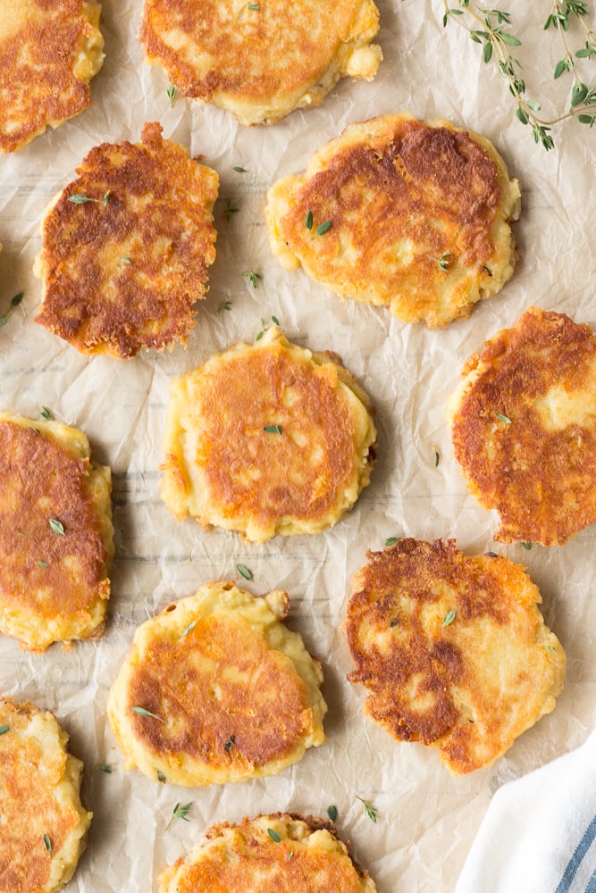 Top down shot of potato pancakes with fresh thyme sprinkled on top, placed on a piece of brown parchment paper.