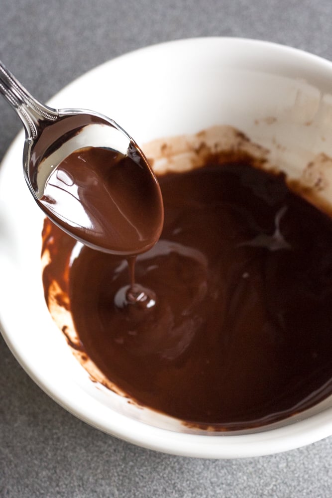 Melted chocolate mixture in a small white bowl with a spoon dipping in it.