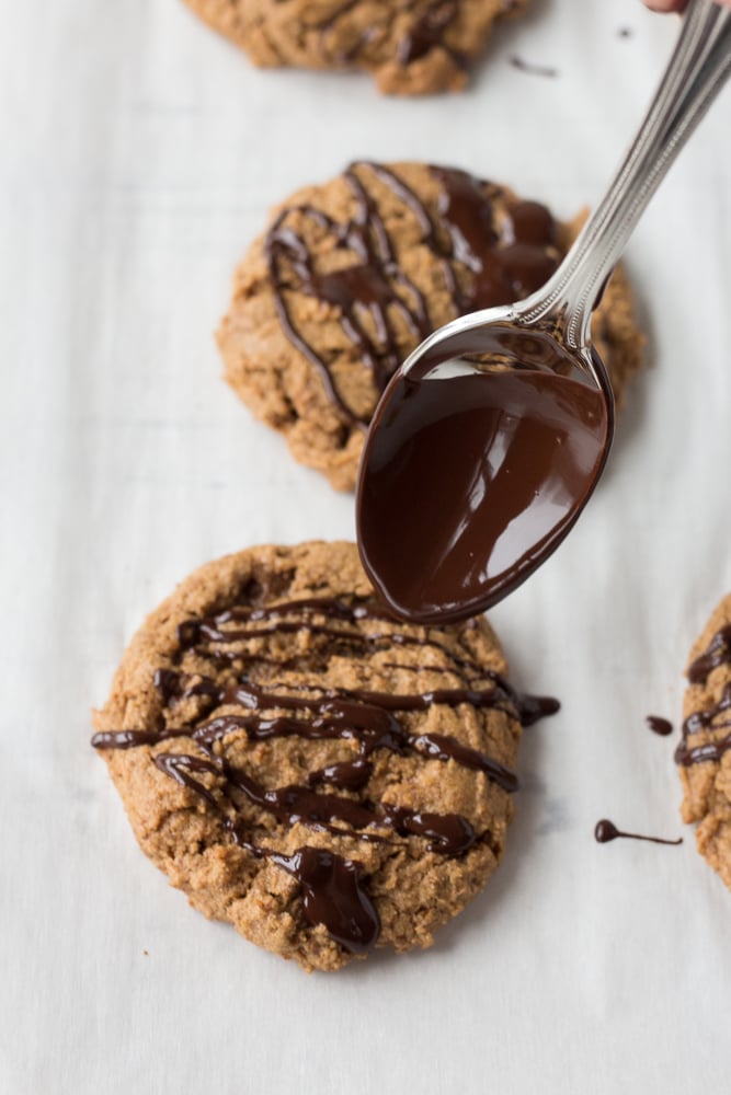 Drizzling chocolate on an almond butter cookie on a white parchment paper.