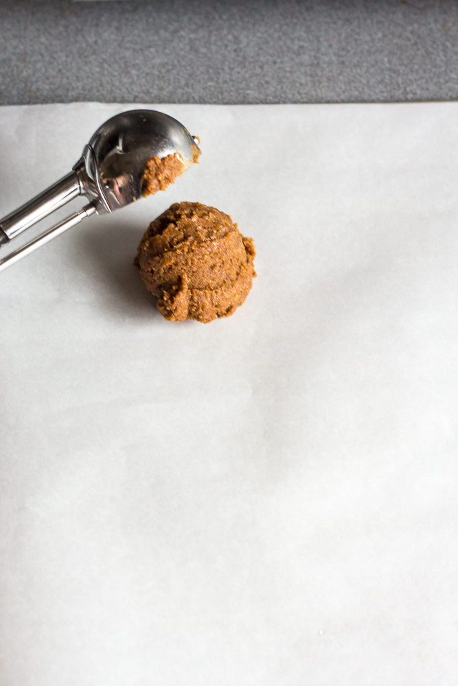 A cookie scoop placing dough on white parchment paper on a cookie sheet.