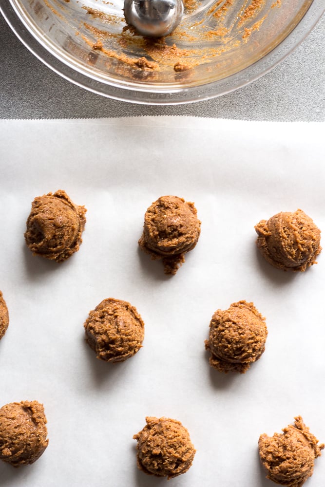 cookie dough balls on parchment paper with an empty bowl beside.