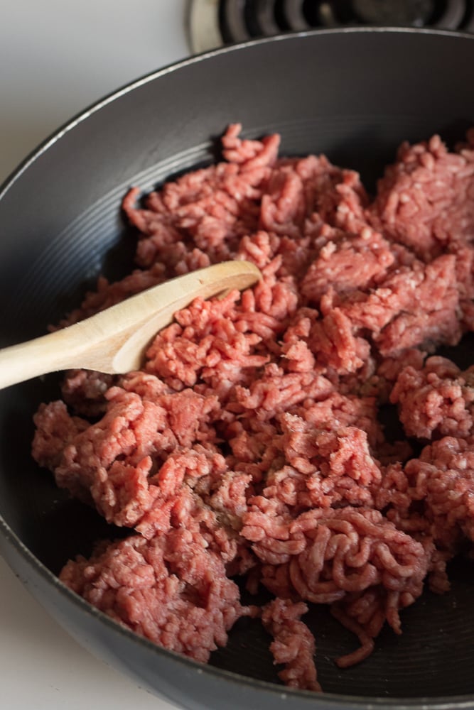 ground beef cooking in a pan with a wooden spoon
