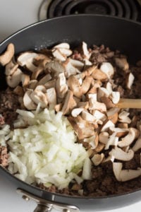 Cut up mushrooms and onion added to a large black pan with ground beef in it.