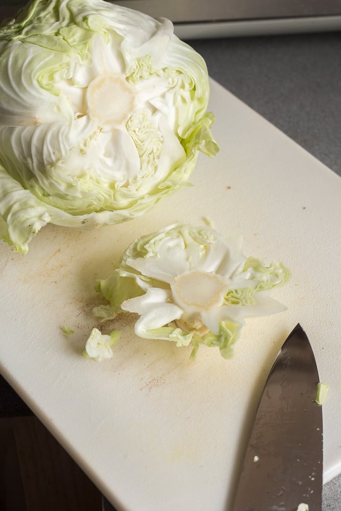 A head of cabbage with its bottom cut off on a white cutting board.
