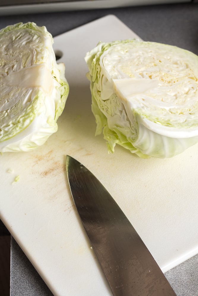 A head of green cabbage sliced in two on a white cutting board.