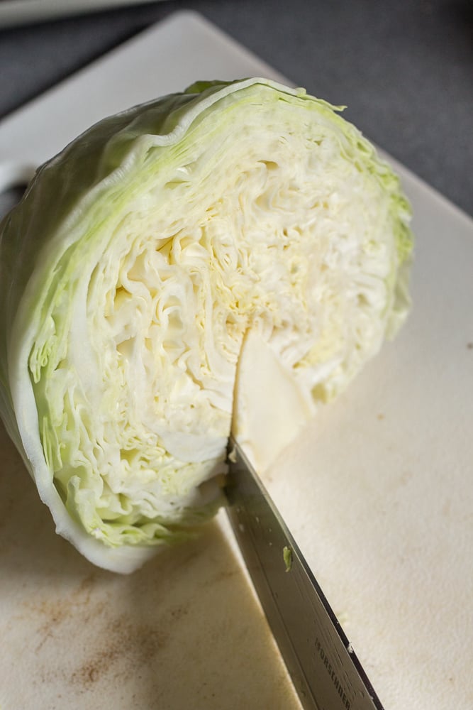 Cutting the core off half a head of green cabbage on a white cutting board.