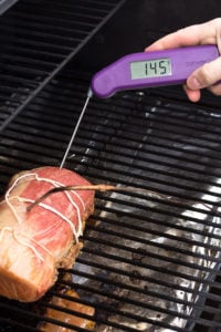 a meat thermometer checking smoked pork loin roast on the grill