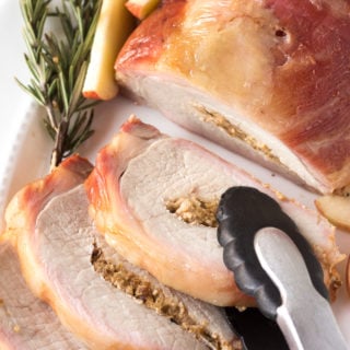 a pair of tongs taking a slice of smoked pork loin roast