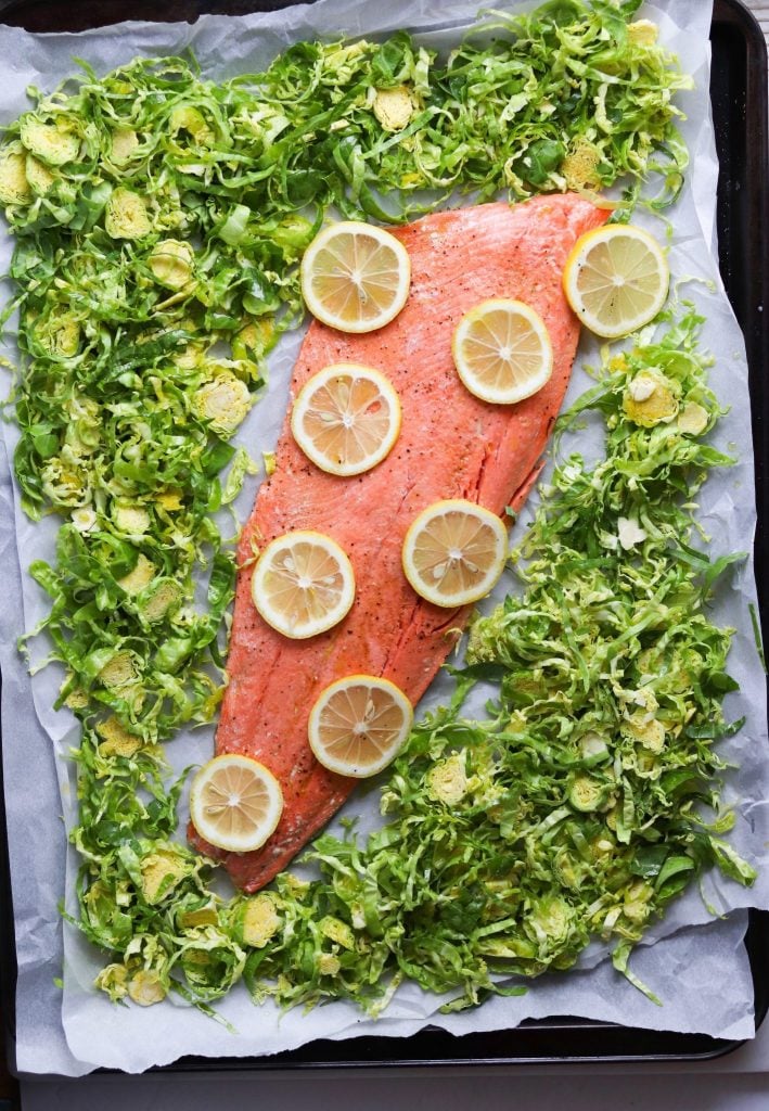 Top down shot of uncooked salmon with lemons and shaved Brussels sprouts on a sheet pan lined with white parchment paper.