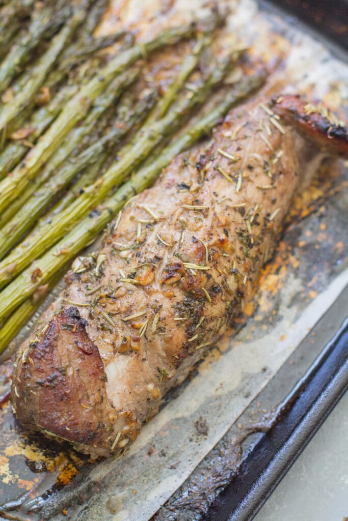 Close up of pork tenderloin and asparagus on a sheet pan.