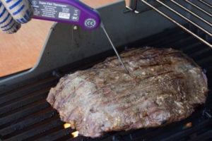 checking internal temperature of flank steak on the grill