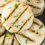 Close up of grilled onions on a gray plate with chopped fresh herbs sprinkled on top.
