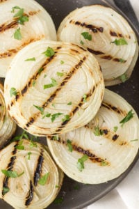 Close up of grilled onions on a gray plate with chopped fresh herbs sprinkled on top.