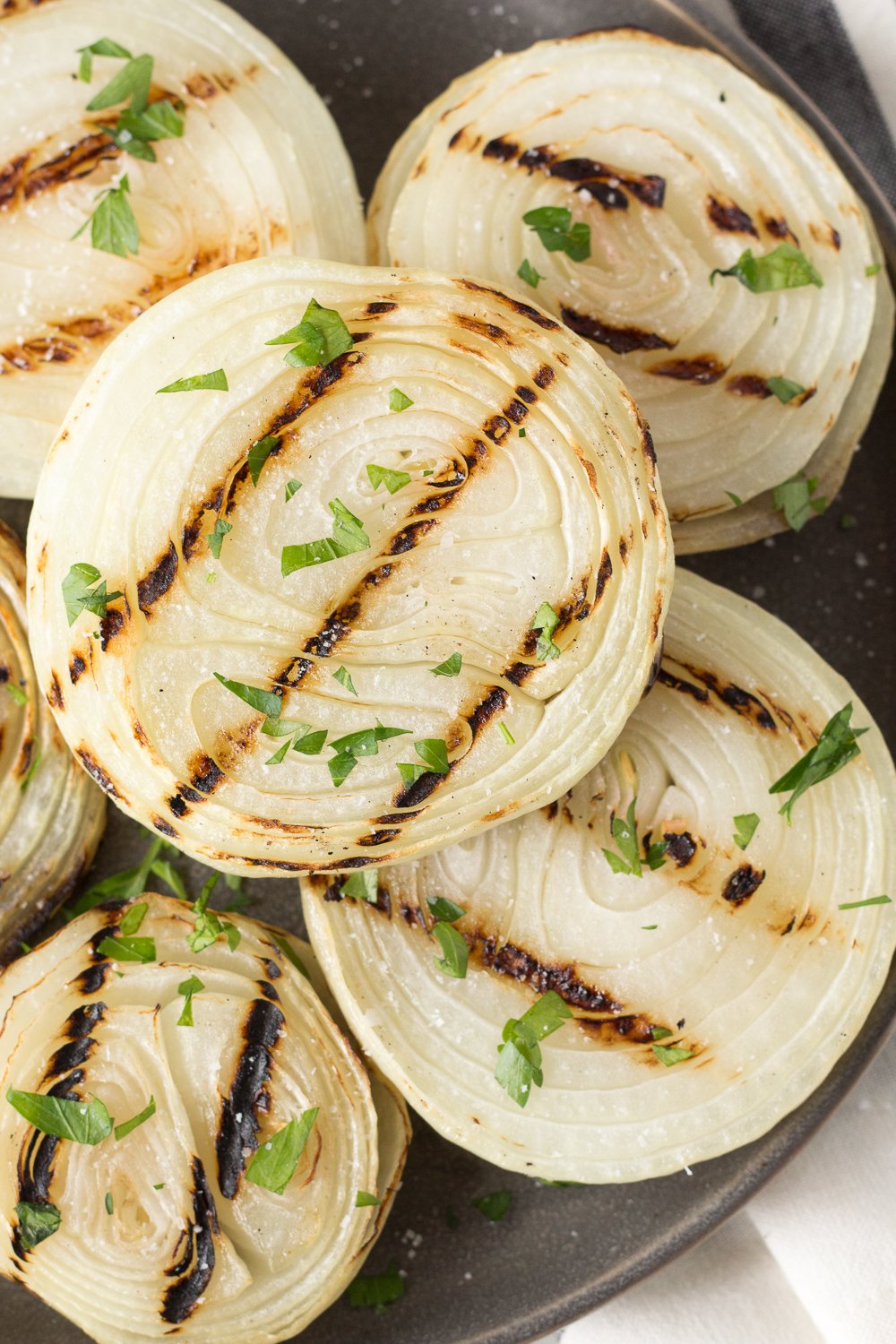 Close up of grilled onions on a gray plate sprinkled with salt and chopped fresh parsley.