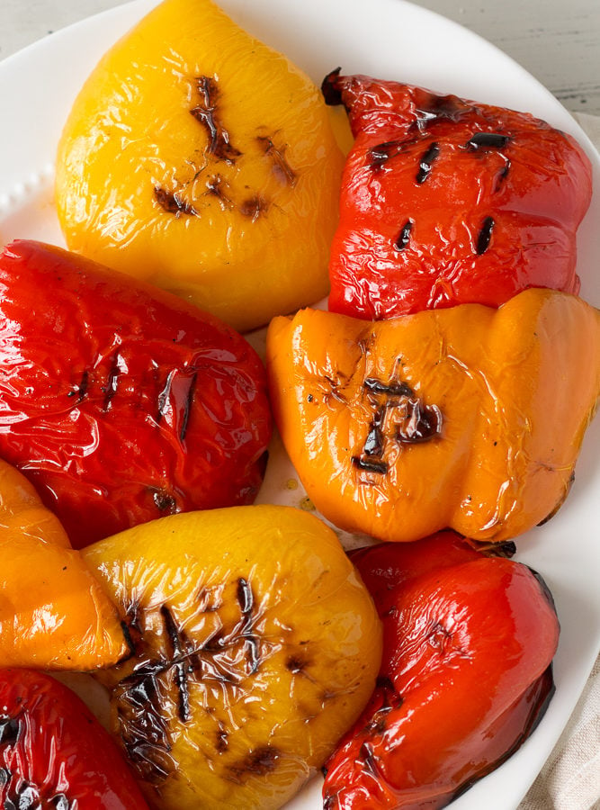 Red, yellow, and orange grilled bell pepper halves on a white platter.