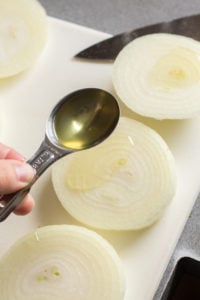 pouring oil on a large slice of an onion