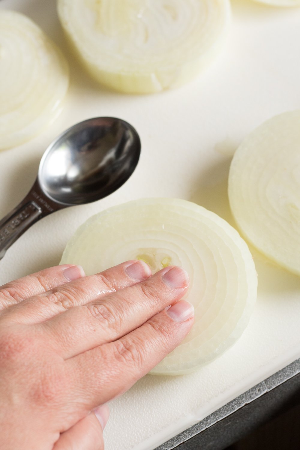 A hand rubbing oil into a large slice of onion on a white cutting board.