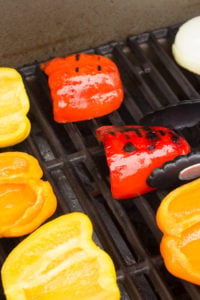 a pair of tongs flipping over grilled bell peppers