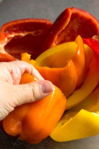 a hand rubbing seasoning into halved bell peppers in a clear bowl