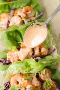 A spoon drizzling an orange sauce on shrimp and coleslaw that's in leaves of butter lettuce.
