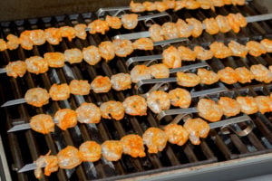 Ten metal skewers of shrimp on a grill.