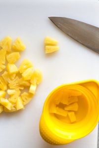 cutting pineapple chunks on a white cutting board