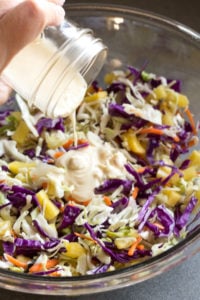 pouring dressing onto pineapple coleslaw