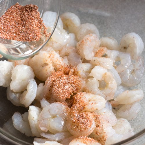 sprinkling seasoning blend on raw shrimp in a bowl