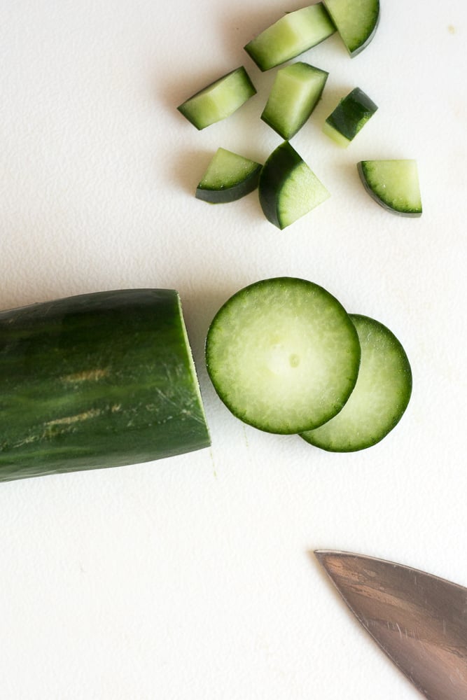 A cucumber being cut into quarters on a white cutting board.