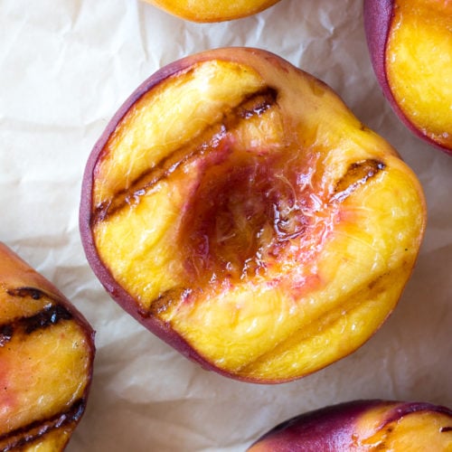 Top down close up of halved grilled peaches on white parchment paper.
