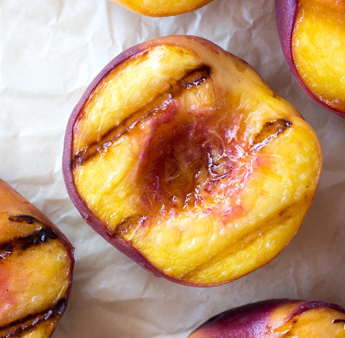 Top down close up of halved grilled peaches on white parchment paper.