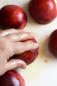rubbing oil on the skin of a peach half