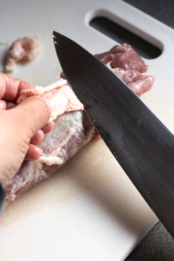 Removing fat from a pork tenderloin with a large sharp knife.