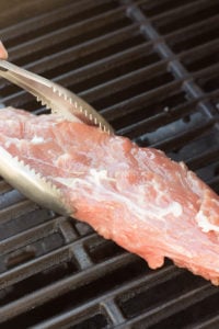 placing pork tenderloin on the grill with tongs