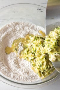 pouring wet zucchini mixture into bowl with dry ingredients