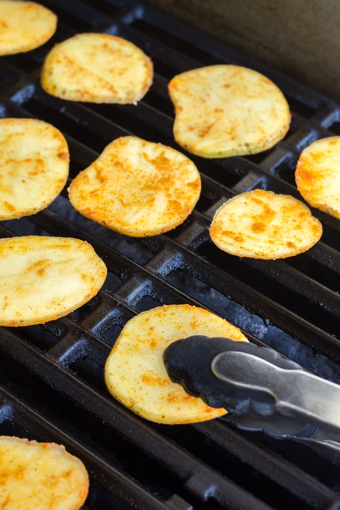 setting sliced potatoes onto a grill with tongs