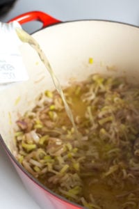 pouring broth onto leeks and shallots on a dutch oven