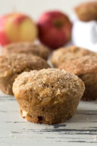 Apple cinnamon muffins on a table with apples in the background.